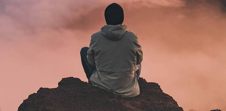 A person sits in quiet contemplation on a rocky outcrop at dusk