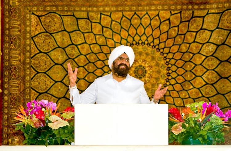 Sant Rajinder Singh Ji Maharaj speaking from a flower-decked podium